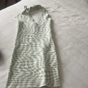 Mintgrön mönstrad halterneckklänning Gina Tricot - Superfin kort klänning från Gina Tricot i mintgrönt och vitt med coolt grafiskt mönster. Halterneck med knyt i nacken och djup v-ringning. Perfekt för sommardagar och ger en fräsch vibe. Materialet känns mjukt och stretchigt.