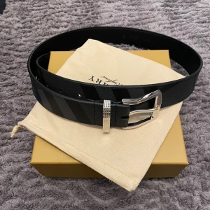 Burberry Läder Bälte - Ett snyggt läder bälte från Burberry. Säljs pga av att den inte passade mig. Längd: 100 cm, utan skärp: 85 cm. 4 hål, medföljer en håltagare, ifall man skulle va intresserad i att göra flera hål. Låda, påse, box och mer medföljer vid köp!