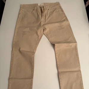 Beige raka jeans från Two men in the world - Snygga beige jeans från Two men in the world med klassisk femficksdesign och raka ben. Jeansen har en neutral, ljusbeige färg och är tillverkade i bomull. Perfekta för en clean och stilren look. Orginal pris:2000kr+ 
