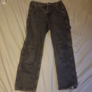 BDG svarta cargojeans W26 L32 - Säljer ett par svarta cargojeans från BDG med raka ben och råa kanter nertill. Jeansen har flera fickor på sidorna och bak, samt klassisk knapp- och dragkedjestängning. Perfekta för en avslappnad streetstil.