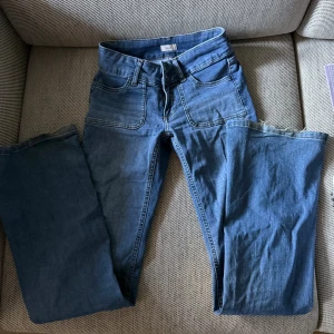 Blå bootcut jeans från Nelly - Snygga blå jeans från Nelly med bootcut passform och låg midja. Jeansen har framfickor med markerade sömmar, dubbla knappar och dragkedja. Baktill finns fickor med coola detaljer. Inga defekter, säljer därför att de inte kommer till användning 