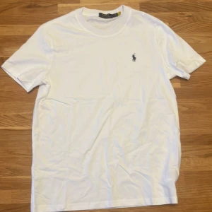 Vit t-shirt från Polo Ralph Lauren - Vit klassisk t-shirt från Polo Ralph Lauren med broderad marinblå logga på bröstet. T-shirten har rund halsringning och korta ärmar. Tillverkad i mjuk bomull för en skön känsla och clean look.