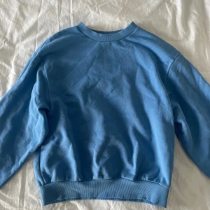 Blå sweatshirt från Gina Tricot XS - En basic blå sweatshirt från Gina Tricot, basically basics-kollektionen. Tröjan har rund hals, ribbade muddar vid ärmslut och nederkant samt mjukt fleecefoder på insidan. Perfekt för chill dagar och enkel att matcha med jeans eller leggings.