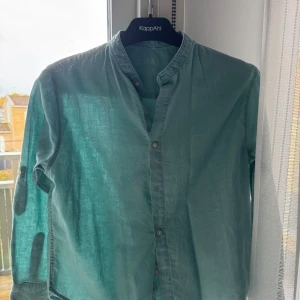 Grön henley skjorta från Zara - Snygg grön henley skjorta från Zara med ståkrage och knappar framtill. Skjortan är långärmad och tillverkad i mjuk bomull, perfekt för dig som gillar enkel och stilren design. Passar dig som vill ha en chill och clean look.