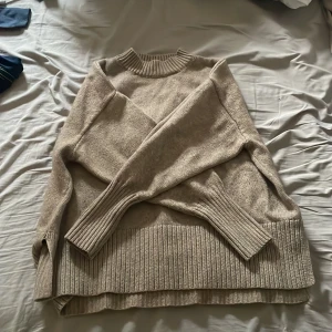 Beige stickad tröja med slits - Säljer en beige stickad tröja med ribbad hög hals och breda ribbade muddar vid ärmslut och nederkant. Tröjan har slitsar på sidorna och en loose passform som ger en chill vibe. Perfekt för lager-på-lager under höst och vinter. Strl L på den men passar super på s/m oversized😊