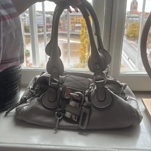 Chloé Paddington handväska i grå skinn - Cool beige Chloé Paddington handväska i mjukt skinn med chunky silverfärgade detaljer, ikoniskt hänglås och kedja med Zadig-berlock (kan köpas till för 200kr). Väskan har dubbla handtag, dragkedja upptill och flera snygga sömmar och nitar som ger en edgy vibe.