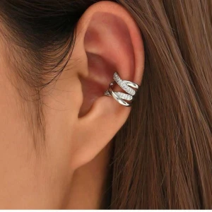 Glittrig silver ear cuff - Snygg ear cuff i silverfärg med glittriga stenar. Designen är flätad med två rader av små kristaller och en slät rad som korsar över. Aldrig använts