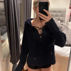 Mörkblå stickad hoodie med snörning - Säljer en mörkblå stickad hoodie från Primark med snygg snörning framtill och huva. Tröjan har grov ribbstickning, långa ärmar och en loose passform. Perfekt för dig som gillar chill och stilren look. Storlek 2XS.