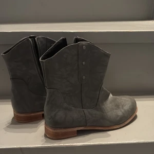 Grå boots med träfärgad sula - Snygga grå boots med träfärgad platt sula och rund tå. Skorna har dragkedja på insidan och dekorativa nitar upptill. Tillverkade i skinnliknande material med matt finish. Perfekta för dig som gillar stilrena och enkla boots med lite edge.