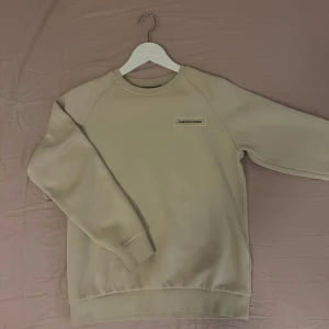Beige Peak Performance sweatshirt - Snygg beige sweatshirt från Peak Performance med broderad logga på bröstet. Tröjan har rund hals, ribbade muddar och är tillverkad i mjuk bomullsblandning. Perfekt för en chill och stilren look.