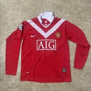 Manchester United långärmad matchtröja - Röd Manchester United fotbollströja från Nike med vita detaljer och AIG-logga på bröstet. Långärmad modell med klassisk krage och klubbmärke broderat på vänster sida. Tillverkad i lätt och ventilerande polyester, perfekt för match eller träning.