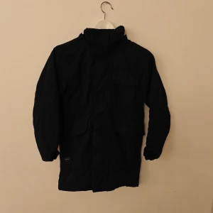 Didriksons vinterjacka - Svart parkas från Didriksons med huva och fuskpäls, flera fickor framtill och broderad logga på bröstet. Jackan har mysigt teddyfoder på insidan och är perfekt för kalla dagar. Klassisk och stilren design som funkar till det mesta.