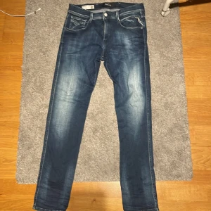 Replay Anbass jeans blå, storlek 30 - Säljer ett par snygga Replay Anbass jeans i blå tvätt med slitningar och kontrastsömmar. Modellen har smal passform, klassiska fem fickor och dragkedjegylf. Perfekta för dig som gillar stilrena och moderna jeans.