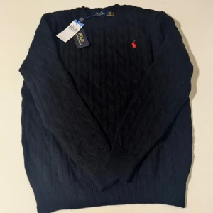 Polo svart tröja  - Svart kabelstickad tröja från Polo Ralph Lauren med klassisk röd broderad logga på bröstet. Jätteskön att bära.
