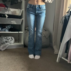 Blå bootcut jeans med låg midja - Snygga blå jeans med bootcut-modell och låg midja. Jeansen har klassiska fickor fram och bak, samt en lätt tvättad look. Perfekta för dig som gillar en avslappnad men trendig stil.