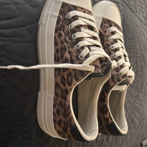 Leopardmönstrade sneakers från Zara - Snygga sneakers från Zara med leopardmönster i bruna och svarta toner. Skorna har vit sula, vita snören. Ovandelen är i textil och sulan i gummi. Perfekta för dig som vill sticka ut med ett coolt djurmönster. Prislapp kvar, storlek 41