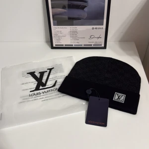 Svart L och V mössa med logga - Svart mössa från L och V med stilren design och uppvikt kant. Märkets ikoniska L och V logga i vitt sitter snyggt framtill på kanten. Mössan är stickad och har en exklusiv känsla, perfekt för dig som vill ha något lyxigt och cleant.