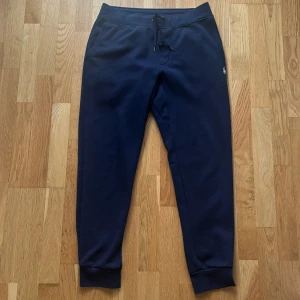 Ralph Lauren Byxor - Snygga marinblå mjukisbyxor från Polo Ralph Lauren med broderad vit logga på höften. Tillverkade i mjukt, dubbelt stickat material för extra komfort. Inga skador eller hål, men kan vara lite noppriga på grund av användning – därav priset. Nypris ca 2000 kr. 