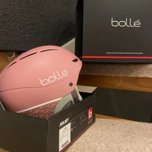 Bollé Juliet hjälm vintage rose - Säljer en snygg och bekväm Bollé Juliet hjälm i färgen vintage rose matt. Hjälmen har ventiler upptill, mjuk grå insida med öronvärmare och justerbart spänne. Baksidan har ett diskret mönster och rem för Googles. Lite skrapad uppe på toppen av hjälmen men inget man märker. Den är även en limited edition, som är köpt i Frankrike💕