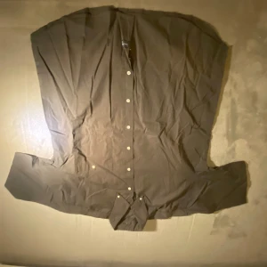 Grå-brun skjorta från Grizzly Collection - Snygg brun-grå skjorta från Grizzly Collection med klassisk krage och vita knappar framtill. Skjortan har lång ärm och broderad logga på insidan av kragen. Materialet känns som bomull och passformen är normal. Perfekt för dig som gillar stilrena och enkla plagg.