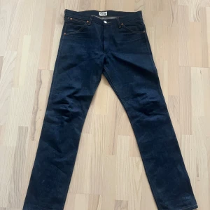 Mörkblå jeans från Wrangler - Snygga mörkblå jeans från Wrangler med klassisk femficksdesign och kontrastsömmar. Modellen har raka ben och normal passform, med tydlig W-söm på bakfickorna och läderpatch med logga. Perfekt för dig som gillar tidlös denimstil.