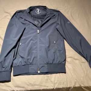 Mörkblå vindjacka från Save the duck - En mörkblå vind/ regn jacka från Save the duck i storlek M. Jackan är mot regn och vind som det står på sista bilden, Den är i väldigt bra skick. Skriv om du har frågor!