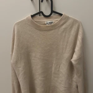 Kashmirtröja Soft Goat - Supermjuk beige tröja från Soft Goat i 100% kashmir. Klassisk rund halsringning, ribbade muddar och lång ärm. Perfekt för dig som gillar stilrena och lyxiga basplagg med en chill vibe. En liten fläck på armen som inte syns så mycket.