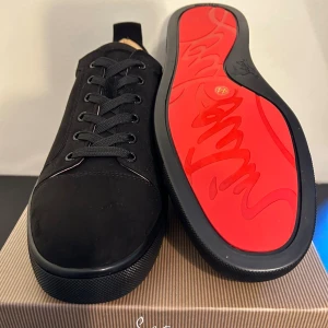 Christian Louboutin svarta sneakers - Svarta sneakers från Christian Louboutin i mocka med klassisk röd sula. Snygg och stilren design med rund tå, svarta skosnören och diskreta detaljer. Perfekta för dig som vill ha en lyxig touch på din outfit.