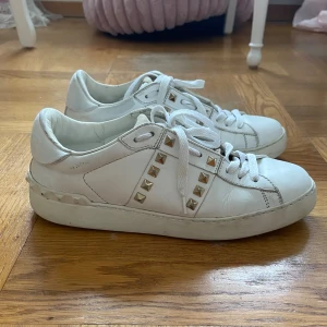 Valentino Rockstud vita sneakers Dam - Vita Valentino Rockstud sneakers i skinn med guldiga nitar på sidorna och runt hälen. Köpta här från Plick tidigare. Klassisk rund tå, platt sula och snörning framtill. Bra skick och väl omhändertagna. På vissa ställen har lite färg flagnat men det är knappt synligt. Hör av dig vid frågor! Samt pris går att diskutera! 