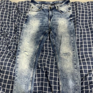 Blå slitna jeans från FSBN, 28/32 - Säljer ett par blå jeans från FSBN med snyggt slitna detaljer och ljus tvätt. Klassisk femficksmodell med dragkedja och knapp. Jeansen har en smal passform och är tillverkade i bomullsmaterial för en bekväm känsla.