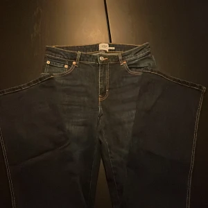 Bootcut jeans 90's från 157, mörkblå - Mörkblå bootcut jeans från 157 med klassisk 90-talsvibe. Snygga kontrastsömmar, femficksmodell och bakfickor med lock och knapp. Jeansen har normal passform och är tillverkade i jeansmaterial med en cool tvätt.