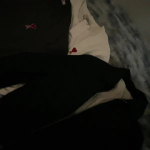 Vit t-shirt från Ami Paris med hjärtdetalj - Vit t-shirt från Ami Paris med röd broderad hjärtdetalj och A på bröstet. Klassisk rund halsringning och korta ärmar. Perfekt för en clean och stilren look.