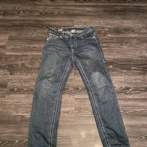 True Religion Joey Super T jeans blå - Säljer ett par blå True Religion Joey Super T jeans med kontrasterande vit söm och stora bakfickor med lock och knapp. Använd 5 gånger och ser nya och är nya å har fortfarande prislapp, Klassisk femficksmodell i jeansmaterial med tydlig logga bak. Snygg passform och coola detaljer som sticker ut.