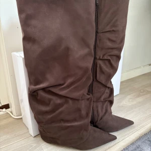 Bruna stövlar med spetsig tå, strl 41 - Säljer ett par bruna stövlar i mocka-look med spetsig tå och låg klack. Stövlarna har dragkedja på insidan och en slouchy, lite rynkad design som ger en cool vibe. Perfekt för dig som gillar statement boots med snygg form. Inköpta på Nelly för 899 kr, tyvärr lite små för mig och därmed inte använda. 