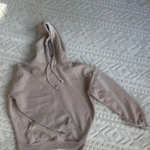 Beige hoodie med huva och ficka - Säljer en beige hoodie med huva och dragsko. Tröjan har en stor magficka och ribbade muddar vid ärmslut och nederkant. 