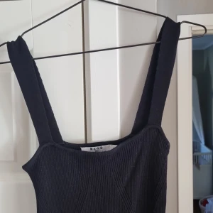 Svart ribbad långklänning från NA-KD - Snygg svart långklänning från NA-KD i ribbat material. Klänningen har breda axelband och en tight passform som framhäver figuren. Perfekt för dig som gillar minimalistisk och stilren look.