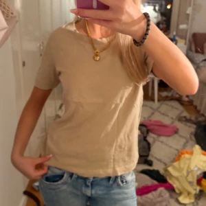 Beige topp - Enkel och stilren beige t-shirt i mjuk bomull. Klassisk rund halsringning och korta ärmar, perfekt till jeans eller shorts. Snygg och clean look som funkar till det mesta.