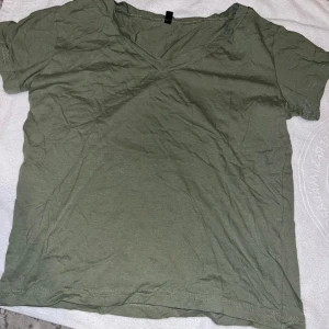 Olivgrön v-ringad t-shirt i bomull - En basic olivgrön t-shirt i storlek S med v-ringning och korta ärmar. Perfekt för en chill och avslappnad stil. Enkel att matcha med jeans eller shorts.