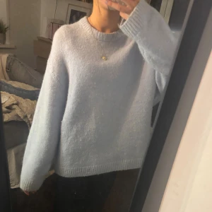Ljusblå stickad tröja från gina - Supermysig ljusblå stickad tröja med rund halsringning och långa ärmar. Tröjan har en relaxed fit och ribbade muddar vid ärmslut och nederkant. Perfekt för lager-på-lager under kyliga dagar.