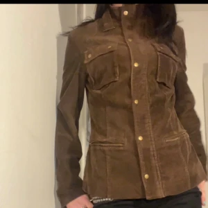 Brun figursydd manchesterjacka  med knappar o spännen - Snygg brun manchesterjacka från Jean Brac med markerad midja, guldiga knappar och dragkedja. Jackan har två bröstfickor med lock och två snedställda fickor framtill. Använt några gånger men inte min stil riktigt