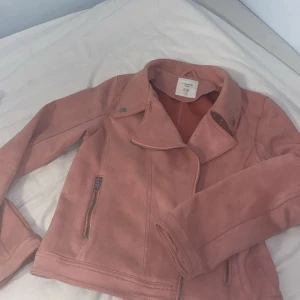 Rosa höstjacka - Aldrig använd!! Snygg rosa mockaliknande från Kappahl med klassisk bikerkrage och dragkedjor framtill. Jackan har långa ärmar och coola sömdetaljer på ryggen. Perfekt för dig som vill sticka ut med en trendig look.