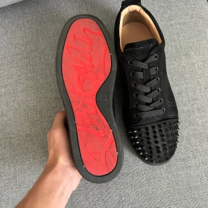 Christian Louboutin svarta sneakers med nitar - Svarta sneakers från Christian Louboutin med ikonisk röd sula och coola svarta nitar på tån. Skorna har snörning och rund tå, tillverkade i skinn och textil. Medföljer dustbag och äkthetskort. Perfekt för dig som gillar edgy designerstil.Det saknas en spik men det finns 3 extra och förutom den skor är jättebra