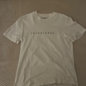 Vit t-shirt från Jack & Jones XS - Vit t-shirt från Jack & Jones Originals i storlek XS. Klassisk modell med rund hals och svart logotyptryck på bröstet. Tillverkad i mjuk bomull för en skön känsla. Perfekt basic-plagg att ha i garderoben.
