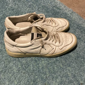 Vita Philippe Model sneakers i skinn booth dust bag finns - Snygga vita sneakers från Philippe Model, handgjorda i Italien. Skorna är i skinn med klassisk låg profil, rund tå och snörning. Yttersulan är beige och svart med tydlig logga undertill. Perfekta för dig som gillar stilrena och tidlösa sneakers.