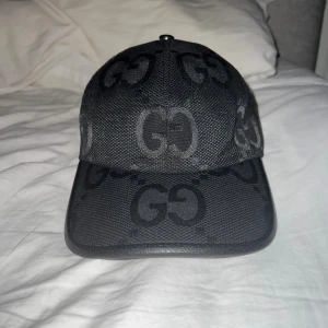 Jumbo GG keps - Säljer en svart keps från Gucci med ikoniskt GG-mönster över hela kepsen. Kepsen har böjd skärm, justerbart spänne i skinn baktill och är tillverkad i ett slitstarkt tyg. Perfekt för dig som vill ha en lyxig och stilren accessoar. Aldrig använd.
