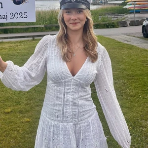 Vit kort klänning från Zara - Supersöt vit kort klänning från Zara med broderade blommor, v-ringning och puffiga långärmar. Klänningen har knappar framtill och volang nertill. Säljs inte längre och är perfekt som skolavslutnings klänning eller bara en sommarklänning!