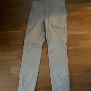 Ljusbeige ridbyxor  - Snygga ljusgrå ridbyxor med snygg horse life logga på benet och halvskodda . Byxorna har bred linning, två bakfickor med knappar och förstärkta benslut. Perfekta för dig som gillar ridning och vill ha stilrena byxor inför tävling. funktionella byxor. Ändas använda en tävling
