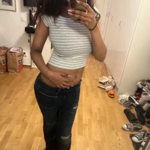 Gråvit randig croppad topp - Säljer en croppad topp i grått och vitt med smala horisontella ränder. Toppen har korta ärmar och är figurnära med rund halsringning. Perfekt för dig som gillar en enkel men snygg stil.