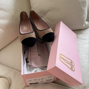 Pretty Ballerinas - Snygga ballerinas från Pretty Ballerinas i beige mocka med svart tå och guldfärgad detalj. Skorna har rund tå och svarta kanter som ger en klassisk look. Perfekta för dig som gillar stilrena och tidlösa skor. Säljes då de tyvärr är för små