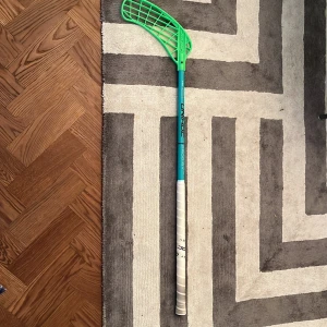 Unihoc Prodigy F36 Innebandyklubba - Unihoc Prodigy F36 innebandyklubba i fint skick. Lätt och tålig klubba med grön blad och turkos skaft, perfekt för både nybörjare och erfarna spelare. Greppet är fräscht och bladet är rakt utan synliga skador. Klubbans skick är mycket bra.